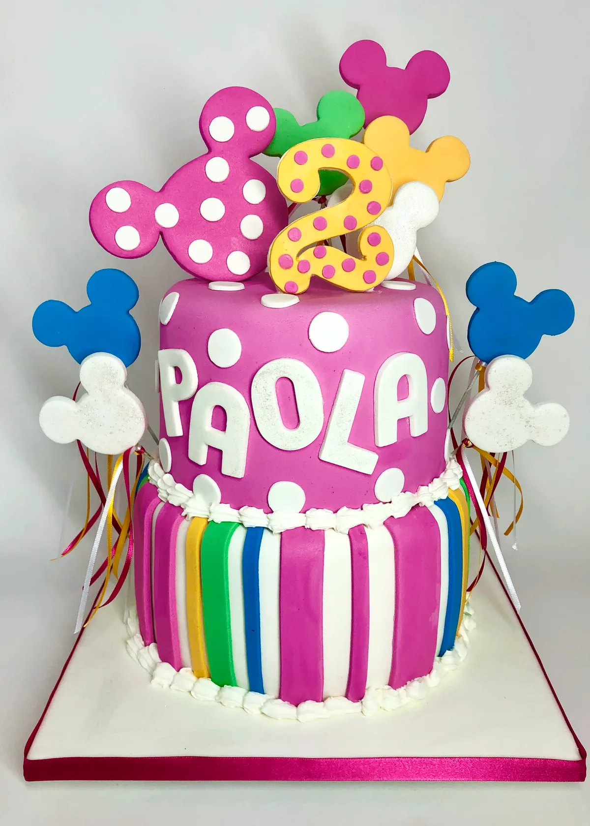 Bolo da Minnie rosa vibrante personalizado com nome PAOLA, listras coloridas e orelhas no topo