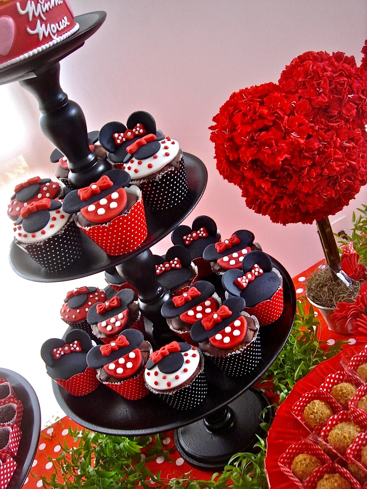 Torre de cupcakes da Minnie em suporte preto com topiaria de flores ao fundo
